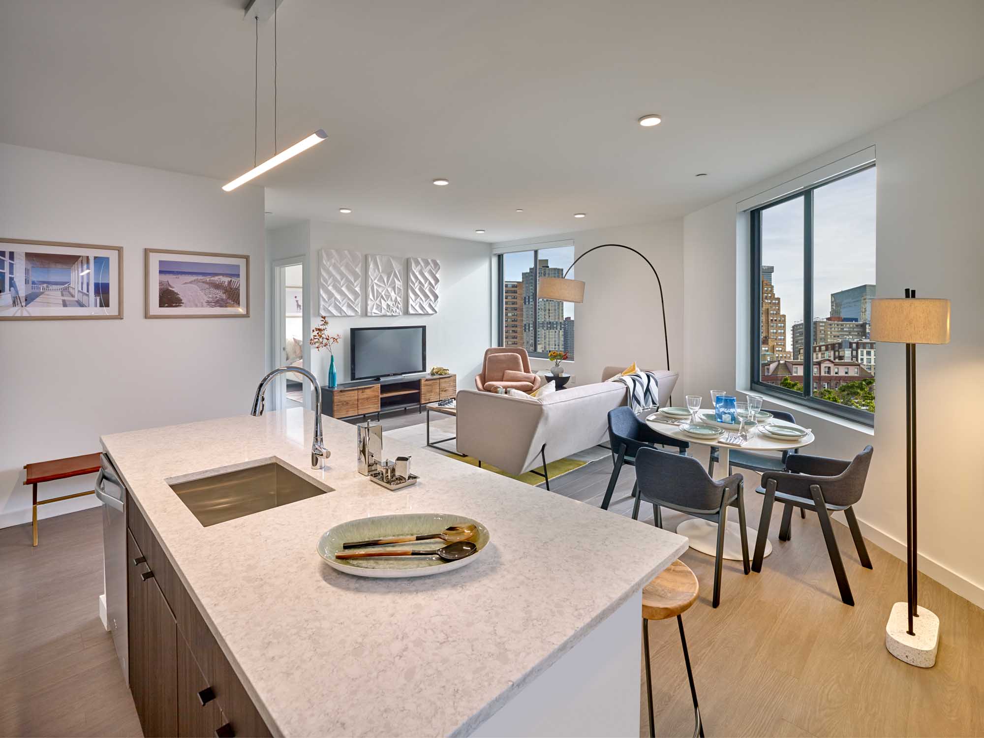 Open layout modern apartment staged with kitchen leading to living and dining areas, sink in island.